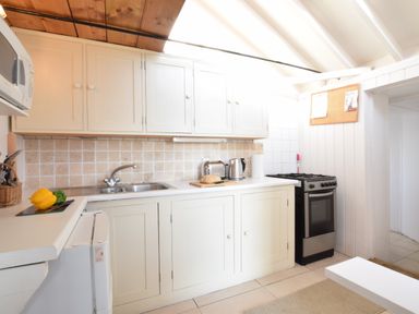 A kitchen with white cabinets a sink a toaster a kettle and a stove at The Old Fisherman's Hut in Southwold