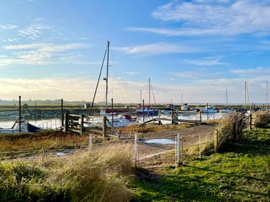A marina with multiple docked sailboats and small boats by a grassy shoreline at The Old Fisherman's Hut in Southwold