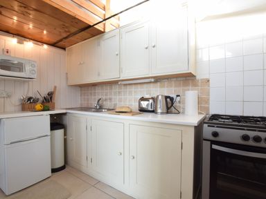 A kitchen with white cabinets a microwave fridge sink toaster kettle and a gas stove at The Old Fisherman's Hut in Southwold