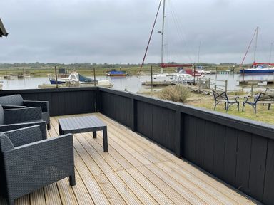 A wooden deck with black chairs and table overlooking a boat dock and sailboats at The Old Fisherman's Hut in Southwold