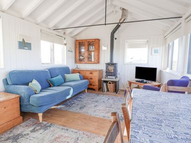 A living room with a blue sofa wood burning stove television and dining table at The Old Fisherman's Hut in Southwold