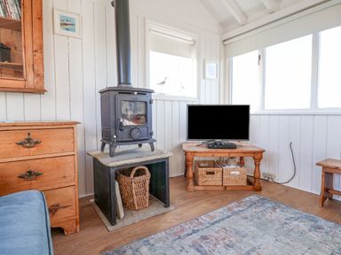 A living room with a wood burning stove a television on a wooden table and wooden drawers at The Old Fisherman's Hut in Southwold