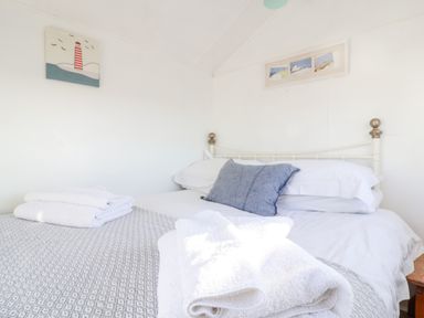 A bedroom with a bed made with white and grey linens and a blue pillow with towels on the bed at The Old Fisherman's Hut in Southwold