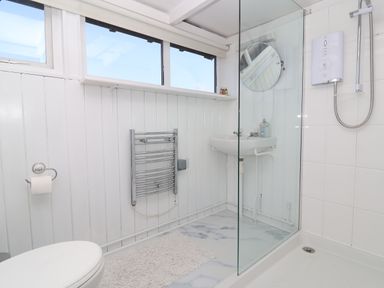 A bathroom with a toilet paper holder towel rail wash basin mirror and shower area at The Old Fisherman's Hut in Southwold