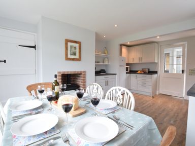 A dining table set with plates and wine glasses in a kitchen with white cabinets and a brick fireplace at Hoist Cottage Walberswick