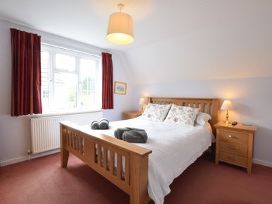 A bedroom with a wooden bed frame bedside tables lamps and a window with red curtains at Hoist Cottage Walberswick