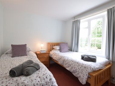 A bedroom with two single beds with floral bedding and grey towels on them at Hoist Cottage Walberswick