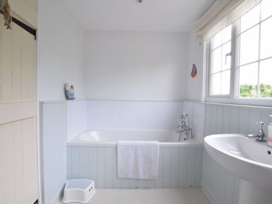 A bathroom with a bathtub a white towel a sink a window and a small step stool at Hoist Cottage Walberswick