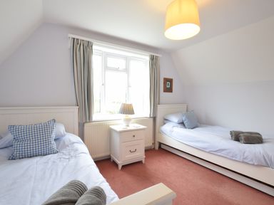 A bedroom with two single beds with blue checked pillows and rolled towels a white nightstand with a lamp between the beds and a window behind at Hoist Cottage Walberswick