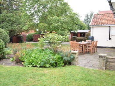 A garden with a patio dining set and assorted plants near a white house at Hoist Cottage Walberswick