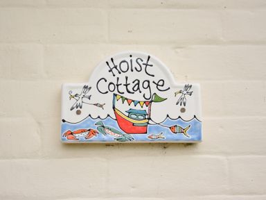 A ceramic house sign with a boat fish crabs and birds reading Hoist Cottage at Hoist Cottage Walberswick