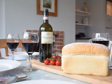 A dining table with a bottle of red wine three glasses of wine a loaf of bread and cherry tomatoes at Hoist Cottage Walberswick