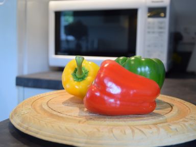 Three bell peppers on a wooden plate in a kitchen with a microwave in the background at Hoist Cottage Walberswick