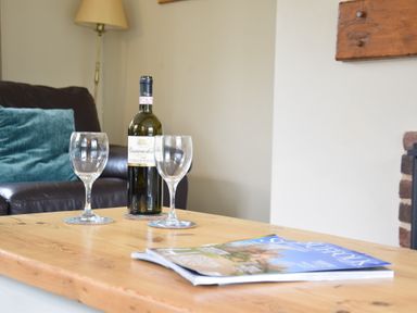 A wooden table with a bottle of wine two wine glasses and a magazine in a living room at Hoist Cottage Walberswick