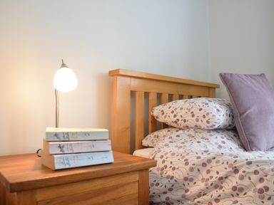 A bedroom with a wooden headboard bedsheets with floral patterns a wooden bedside table with books and a small lamp at Hoist Cottage Walberswick