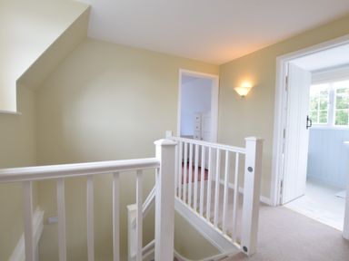 A stair landing with white railing and doorways leading to other rooms at Hoist Cottage Walberswick