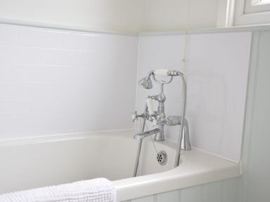 A bathroom with a white bathtub and a chrome faucet with handheld shower at Hoist Cottage Walberswick