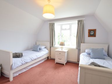 A bedroom with two single beds a nightstand with a lamp and a window with curtains at Hoist Cottage Walberswick