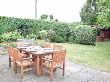 An outdoor patio with a wooden dining table and six chairs set with plates in a garden at Hoist Cottage Walberswick