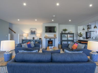 A living room with blue sofas a wood burning stove and a TV at Sea Green Cottage Walberswick