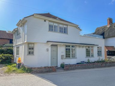 A white two-story house with green windows and door beside a road at Sea Green Cottage Walberswick