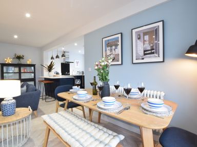 A dining area with a wooden table set for six and a kitchen with bar stools in the background at Sea Green Cottage Walberswick