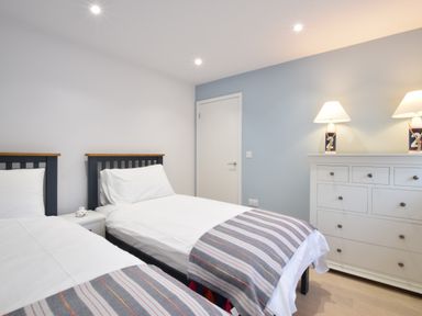 A bedroom with two single beds a white dresser with two lamps and a closed door at Sea Green Cottage Walberswick