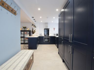 A kitchen with blue cabinets a white countertop pendant lights and a bench at Sea Green Cottage Walberswick