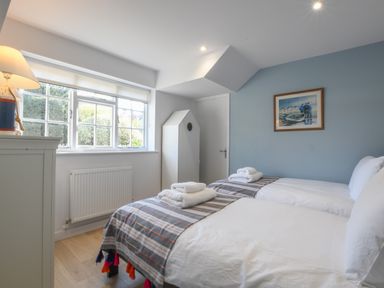 A bedroom with two single beds, towels on beds, a window, a lamp, and a painting on a blue wall at Sea Green Cottage Walberswick
