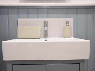 A bathroom sink with a chrome faucet a soap dispenser and a matching container on a gray cabinet