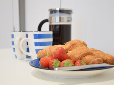 A plate with croissants and strawberries next to two striped cups and a French press with coffee
