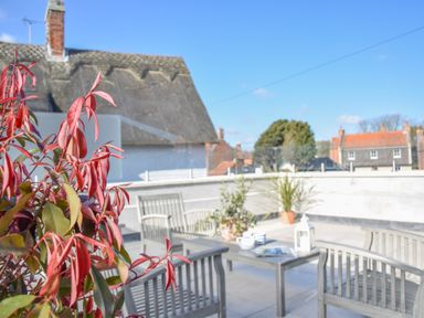 A rooftop terrace with wooden chairs and table with plants and a lantern Sea Green Cottage Walberswick