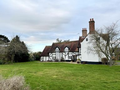 A large house with timber framing and multiple chimneys on a grass lawn with leafless trees at Church Farmhouse Cookley Near Halesworth