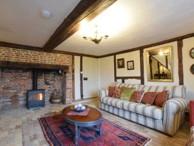 A living room with a striped sofa and cushions a coffee table a rug a wood burning stove in a brick fireplace and framed pictures at Church Farmhouse Cookley Near Halesworth