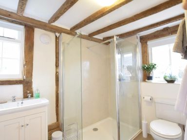 A bathroom with a shower enclosure, white sink cabinet, toilet, and windows with plants on the sill at Church Farmhouse, Cookley Near Halesworth