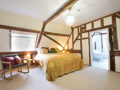 A bedroom with a bed a rocking chair a small table with a lamp and an open door leading to a bathroom at Church Farmhouse Cookley Near Halesworth