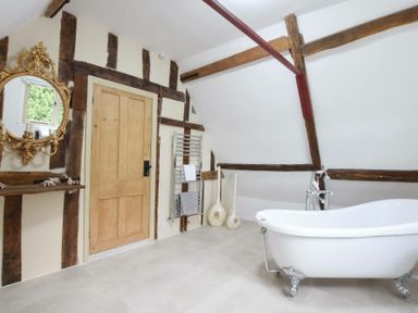 A bathroom with a freestanding bathtub wooden door gold mirror and decorative vases at Church Farmhouse Cookley Near Halesworth