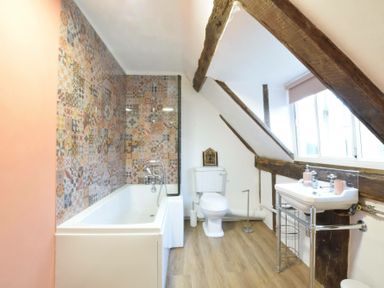 A bathroom with a bathtub and patterned tile wall a toilet and a sink with exposed wooden beams at Church Farmhouse Cookley Near Halesworth