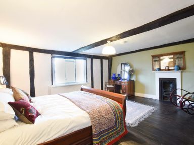 A bedroom with a wooden bed, a dresser with a mirror, a fireplace, and a rocking chair at Church Farmhouse Cookley Near Halesworth