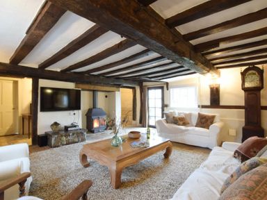 A living room with exposed wooden beams a wood burning stove and white sofas at Church Farmhouse Cookley Near Halesworth