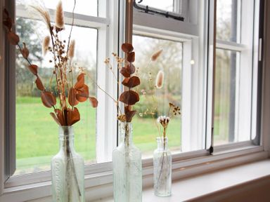 Three glass bottles with dried flowers on a windowsill with a garden view outside at Church Farmhouse Cookley Near Halesworth