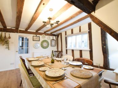 A dining room with a wooden table set with plates, glasses, and wine bottle and a wall with clocks at Church Farmhouse, Cookley Near Halesworth