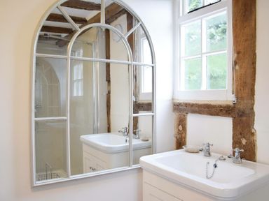 A bathroom with a white sink wooden framed window and arched mirror at Church Farmhouse Cookley Near Halesworth