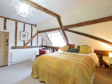 A bedroom with wooden beams a bed with pillows and blankets a chair with cushions and a window at Church Farmhouse Cookley Near Halesworth