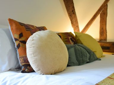 A bed with multiple patterned and textured cushions and wooden beams on the wall at Church Farmhouse Cookley Near Halesworth