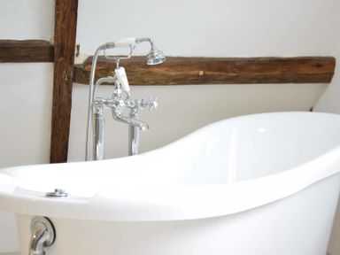 A white freestanding bathtub with chrome faucet and wooden beams on wall at Church Farmhouse Cookley Near Halesworth