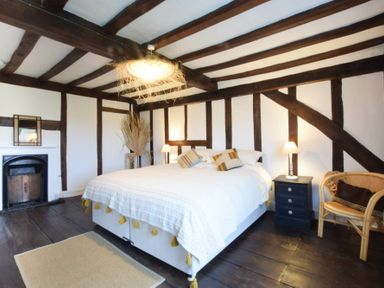 A bedroom with wooden beams a bed bedside tables lamps a fireplace and a chair at Church Farmhouse Cookley Near Halesworth