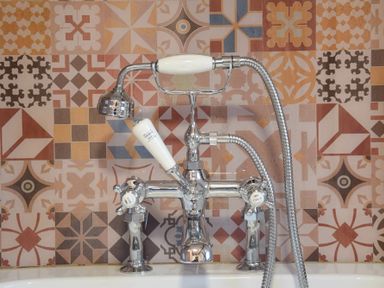 A bathtub faucet with hot and cold handles and a handheld showerhead against patterned tile wall at Church Farmhouse Cookley Near Halesworth