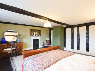 A bedroom with a wooden bed, green wardrobe, rocking chair, fireplace, dressing table, and mirror at Church Farmhouse in Cookley Near Halesworth