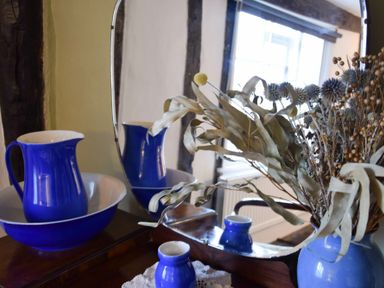 A wooden surface with a blue pitcher and basin and a blue vase with dried flowers in front of a mirror at Church Farmhouse Cookley Near Halesworth